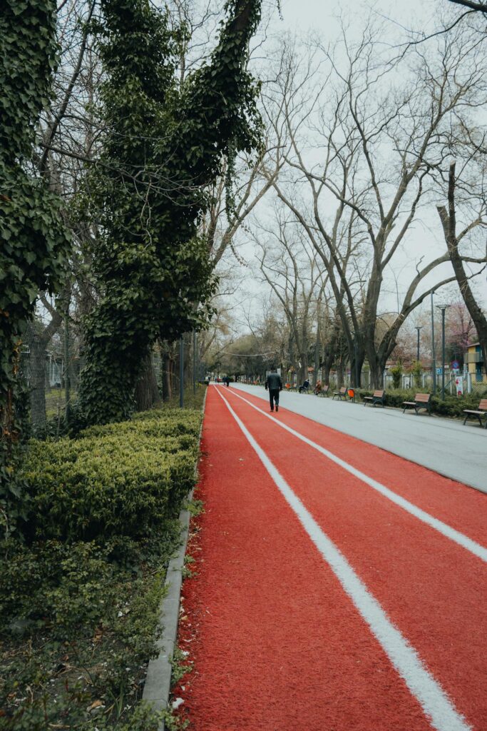 A person walking along a red running track in a tree-lined park, perfect for leisure and exercise.